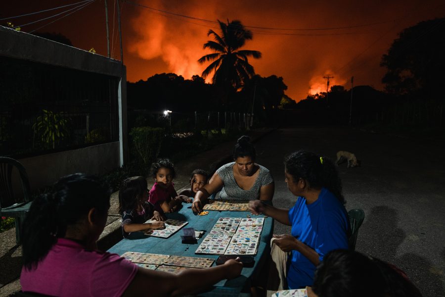 FOTOSERIE, SÜDAMERIKA Roter Himmel, grünes Wasser. PUNTA DE MATA, VENEZUELA - NOVEMBER 5, 2022: Neighbors play board games under a sky lit by gas flares. (© Adriana Loureiro Fernandez für The New York Times, in Zusammenarbeit mit Isayen Herrera und Sheyla Urdaneta)